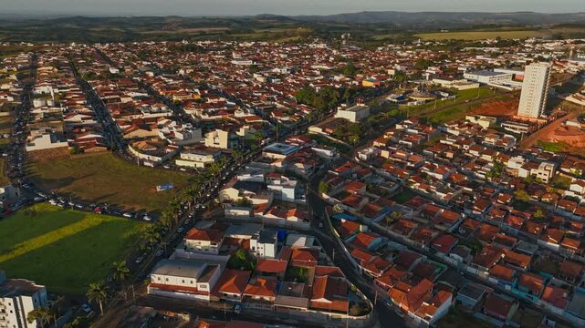 High-angle aerial view of a sprawling suburban city landscape during the golden hour, showcasing dense residential neighborhoods, urban infrastructure, and green spaces under a warm sunset light