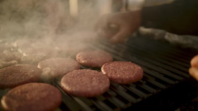 Juicy beef burger patties grilling on a hot outdoor barbecue grill with rising smoke and steam during a summer cookout or street food festival event with warm natural lighting