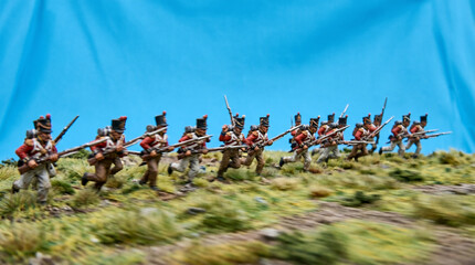 Fototapeta premium March of Time: A regiment of 19th-century soldiers in red uniforms advance across a grassy incline, muskets at the ready, evoking a sense of historical military action and discipline.