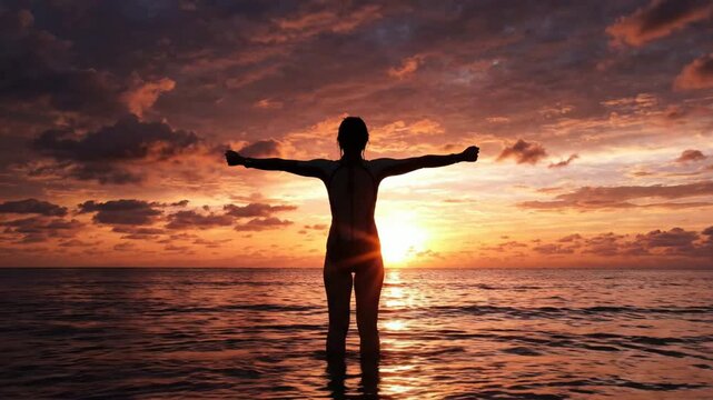 Woman in wetsuit celebrating success with arms raised at sunset on tropical beach silhouette ocean
