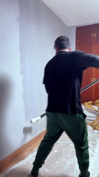 Man painting a room wall with a roller during home renovation and improvement work