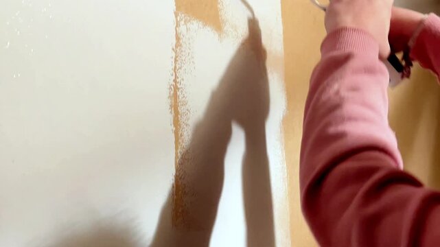 House painter applying white paint on wall with roller during renovation work