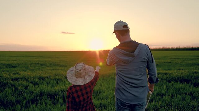 Dad child son hold hands in field. Father, child walk on field, sky sunset. Kid boy, dad go hand in hand, field corn sprouts. Family farming business. Agricultural industry. Growing corn, organic food
