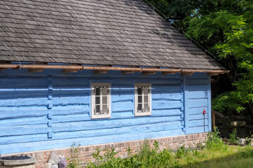 Drewniany niebieski dom w Krakowie, prezentujący XIX-wieczny styl architektoniczny Konstrukcja zbudowana jest z poziomych bali pomalowanych na wyrazisty niebieski kolor Ma białe okienka i dach zgontem © Grzegorz