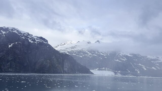 Brash ice drifts past a distant tidewater glacier below cloudy peaks
