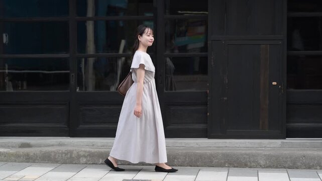 古い町並みの格子戸の前を歩きながら見上げる白いワンピースの若い女性（一人旅・散策）
