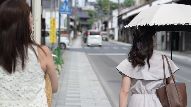 古い城下町の風情ある町並みを日傘を差して観光する職場の上司と部下の女性（後ろ姿）