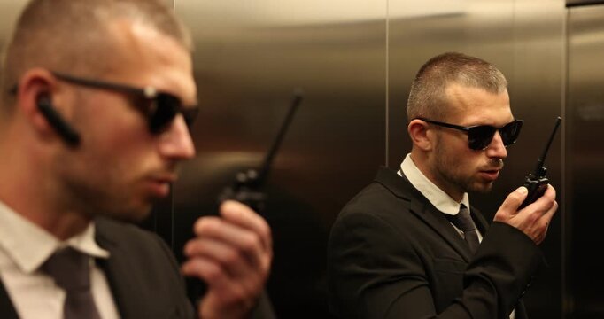 Bodyguard in suit with earpiece using walkie talkie in elevator
