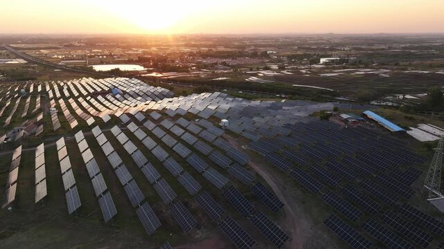 Aerial view of a large-scale photovoltaic power station during sunset with orderly solar panels reflecting golden light
