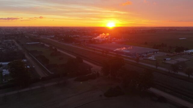 F&aacute;brica industrial con chimeneas emitiendo humo en un pueblo rural al amanecer. Industria, producci&oacute;n, energ&iacute;a, desarrollo econ&oacute;mico, trabajo, infraestructura, paisaje rural