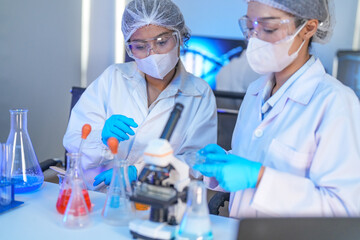 Fototapeta premium Scientists in lab coats and masks examine samples with a microscope and test tubes in a modern research laboratory.