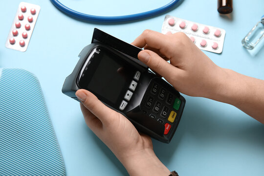 Female hands with payment terminal, credit card and medicines on color background, closeup