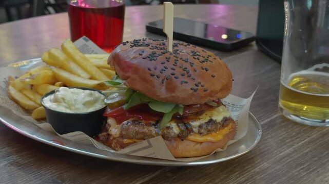 Juicy cheeseburger with fries, creamy dip, and beer served on tray in casual restaurant