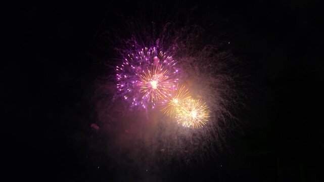 Vibrant multicolored fireworks explode in the dark night sky at a large scale festive event. Rich, bright flashes create an amazing spectacle
