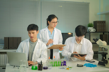 Fototapeta premium Research team in lab coats analyzing test samples and recording data with laptop and tablet in a modern laboratory environment