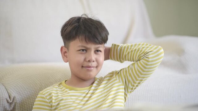 Confused Asian schoolboy scratching hair thinking hard before smiling after solving difficult study problem. Smart preteen pupil overcoming challenge in modern online education course