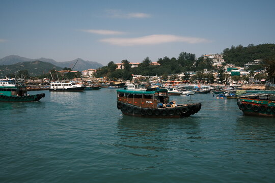 View of traditional sampan boats and vessels anchored in the harbor with lush hills and buildings in the background in Hong Kong, Hong Kong.