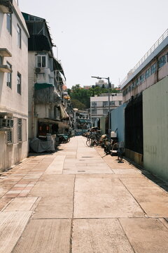 View of a narrow street in Hong Kong flanked by residential buildings with air conditioning units and a long wall under a clear sky in Hong Kong, Hong Kong.