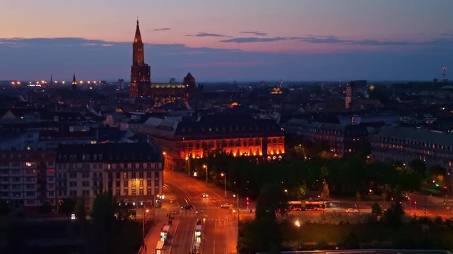Strasbourg Cathedral dominates the skyline of Strasbourg, Bas Rhin, Grand Est, France, surrounded by illuminated streets and historic architecture during blue hour, drone ascent and forward push-in