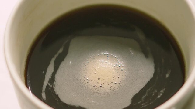 Hypnotising Coffee Swirling in Slow Motion in Ceramic White Mug. High Caffeine Hot Morning Drink.