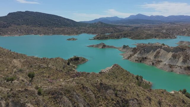 Drone aerial view of the turquoise waters of Embalse de Negrat&iacute;n surrounded by rugged hills and badlands terrain in Andalusia, Spain