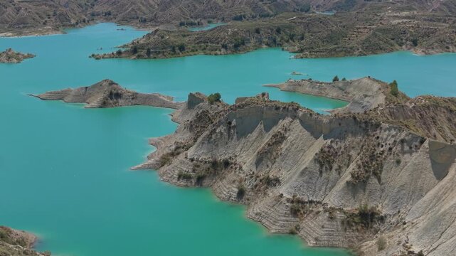 Drone aerial footage of eroded badlands peninsulas surrounded by turquoise waters in Embalse de Negrat&iacute;n, Andalusia, Spain