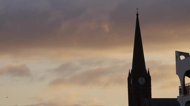 Slow motion bird flying past a church spire against a dramatic sunrise sky. Captured at dawn in Largs, Scotland, with atmospheric clouds and warm early morning light