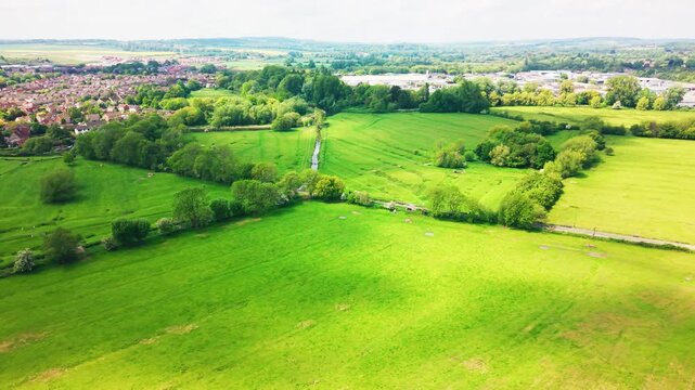 Aerial drone footage of Salisbury Water Meadows in Wiltshire, showing open green fields, tree lines, river channels, countryside, nearby housing and the wider rural landscape. Useful for themes of UK