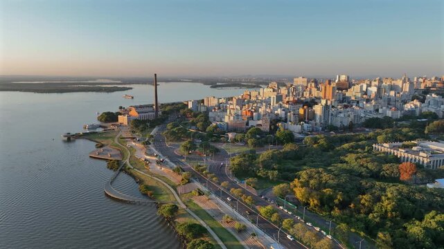 Aerial establishing scene of Porto Alegre's city skyline and riverfront park at golden hour