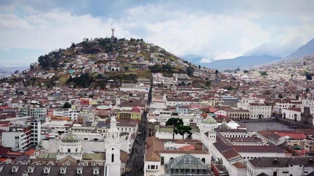 Quito, Ecuador. Aerial view of "Panecillo" town beneath cloudy skies.Blending old and new. Vibrant rooftops contrast with gray stone structures. Mountains loom in the distance