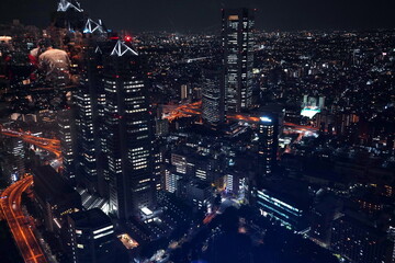 夜の都会風景。高層ビル群が灯りで輝き、道路には走行車の光の痕跡が広がる。 © BRUCE