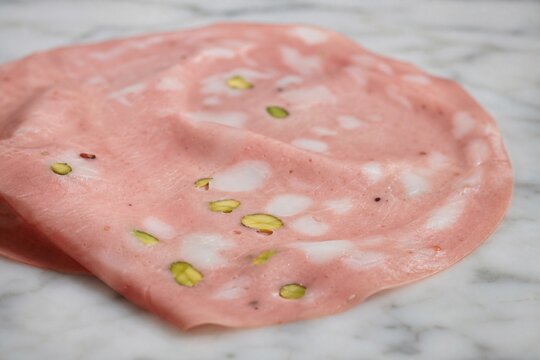Slice of mortadella with pistachio pieces on marble surface, close-up.