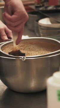 Vertical video. Professional kitchen. Hand cooking. Chef grinding hot mass in metal bowl stirring with spatula. Soft liquid meal puree food in sieve.