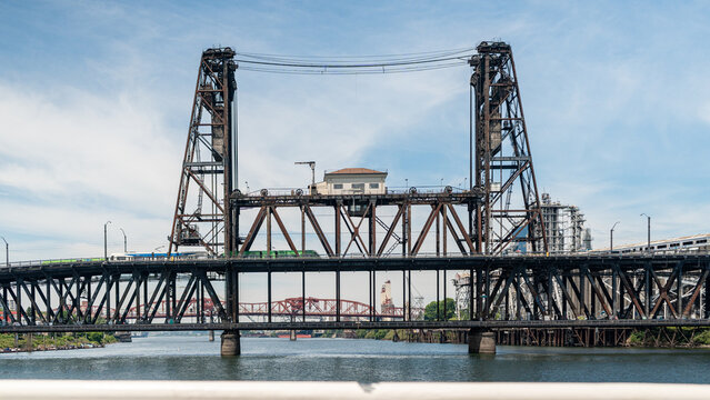View of the historic Steel Bridge crossing the Willamette River with a train passing over the structure under a clear blue sky in Portland, Oregon, United States.