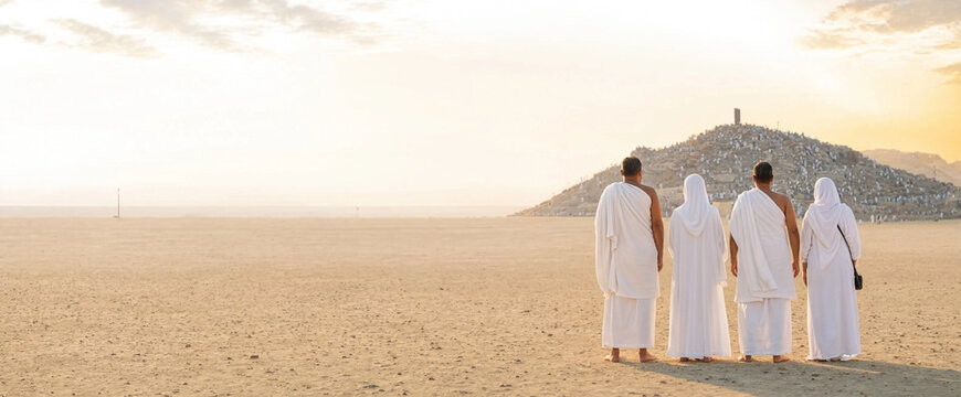 Group of four pilgrims walking together across a sandy plain toward distant hill at sunrise. The figures wear traditional white robes and walk in a calm, contemplative mood.