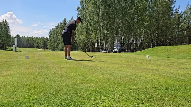 Swinging a golf club on a sunny day at a golf course with trees in the background and a clear sky