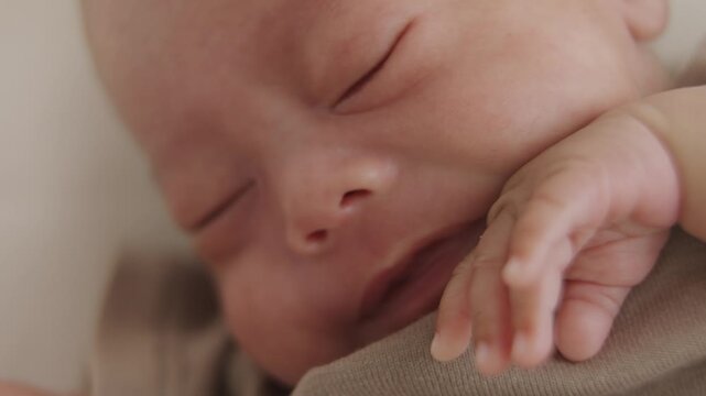 Newborn Expressing Discomfort: A close-up shot of a newborn baby's face showing an expression of discomfort or fussiness, with its arm raised, lying on a patterned surface.