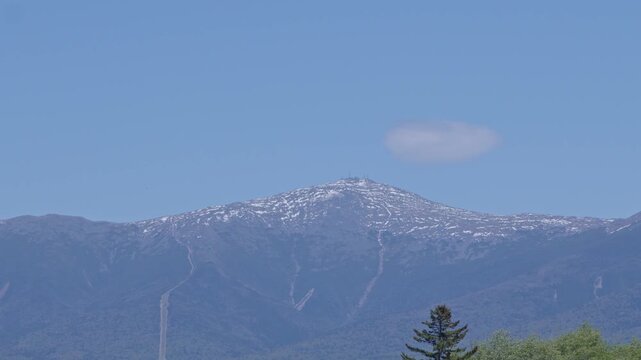View of distant Monte Washington with patches of snow and single cloud in White Mountain National Forest, United States. Static shot, copy space