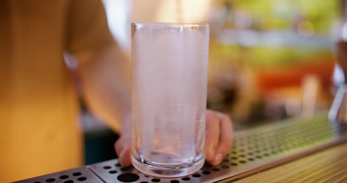 Preparing beverage. Stirring ice. Barkeeper rotating frozen cube in tall glass with spoon on pub counter. Cooling for refreshing drink.