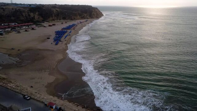 A smooth, fluid drone shot of part of the structure of the artisanal pier of San Mateo, a wave of marine undertow flows in the blue sea while focusing on the dry cliffs that end at the beach of San Ma