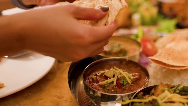 Hands Tearing Naan Bread to Dip in Indian Curry Thali