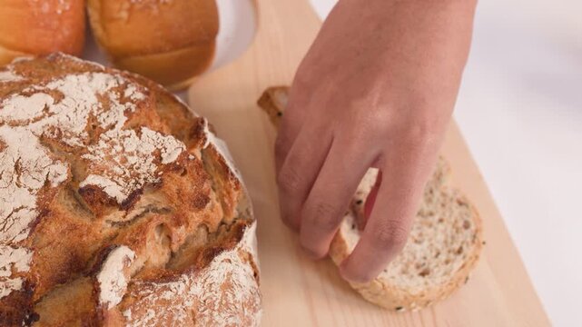 Hand Placing Fresh Sliced Multigrain Bread on Wooden Cutting Board