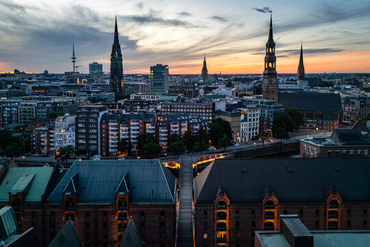 Aerial view of the historic Speicherstadt district with red-brick warehouses and canals, set against the Hamburg skyline at sunset with church spires in Hamburg, Hamburg, Germany.