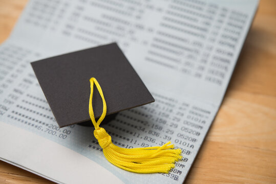 Close up mortarboard on deposit account book bank with wooden table background. Money savings management and planning for education, tuition, repayment student loan or debt and so on concept.