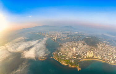 Fototapeta premium Panoramic sunrise view over Nha Trang City, Vietnam, with low clouds drifting across the mountains and coastline. The warm morning light, misty atmosphere, and urban landscape create a stunning scene 