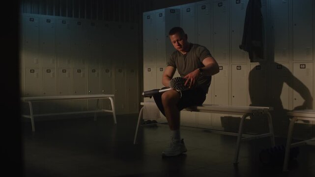 Dedicated Athlete With Physical Disability Sits in Gym Locker Room, Tying Laces of Sports Shoe on Prosthetic Leg, Preparing for Active Workout. Concept of Determination and Adaptive Fitness.