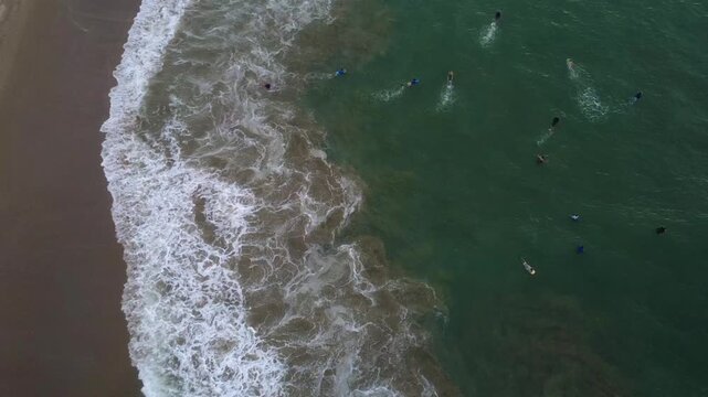 Aerial drone shot of surfers paddling on the light green waters of San Mateo beach, as they wait for the wave and share the warm midday weather in Ecuador, South America