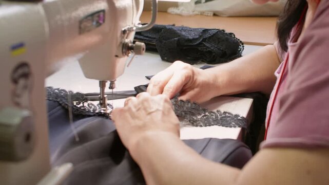 Clothing production. Sewing lace. Dressmaker hand attaching garnish to black fabric corset. Manufacturing industry professional equipment.