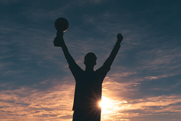Fototapeta premium Man holding trophy in sunset silhouette.