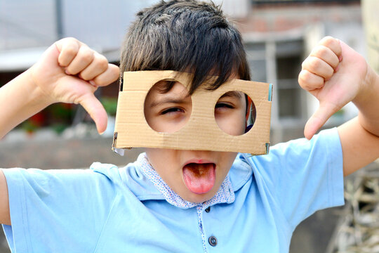 Latin kid wearing huge cardboard glasses with tongue out and thumps down.